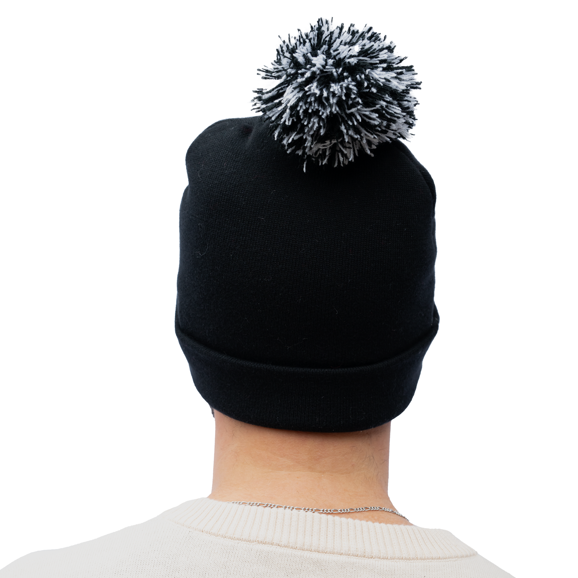 A person is seen from the back against a white background, wearing the Guinness Holiday Toucan Beanie by Guinness Webstore US, a black beanie topped with a distinctive black and white pompom, echoing the style of a classic winter wardrobe essential.