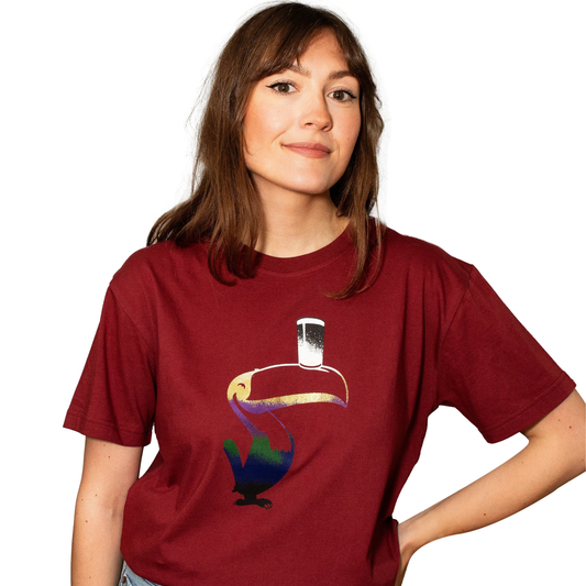 A woman wears the Guinness Liquid Toucan Tee - Red by Guinness, featuring a stylized toucan with a pint glass on its beak, standing against a white background.