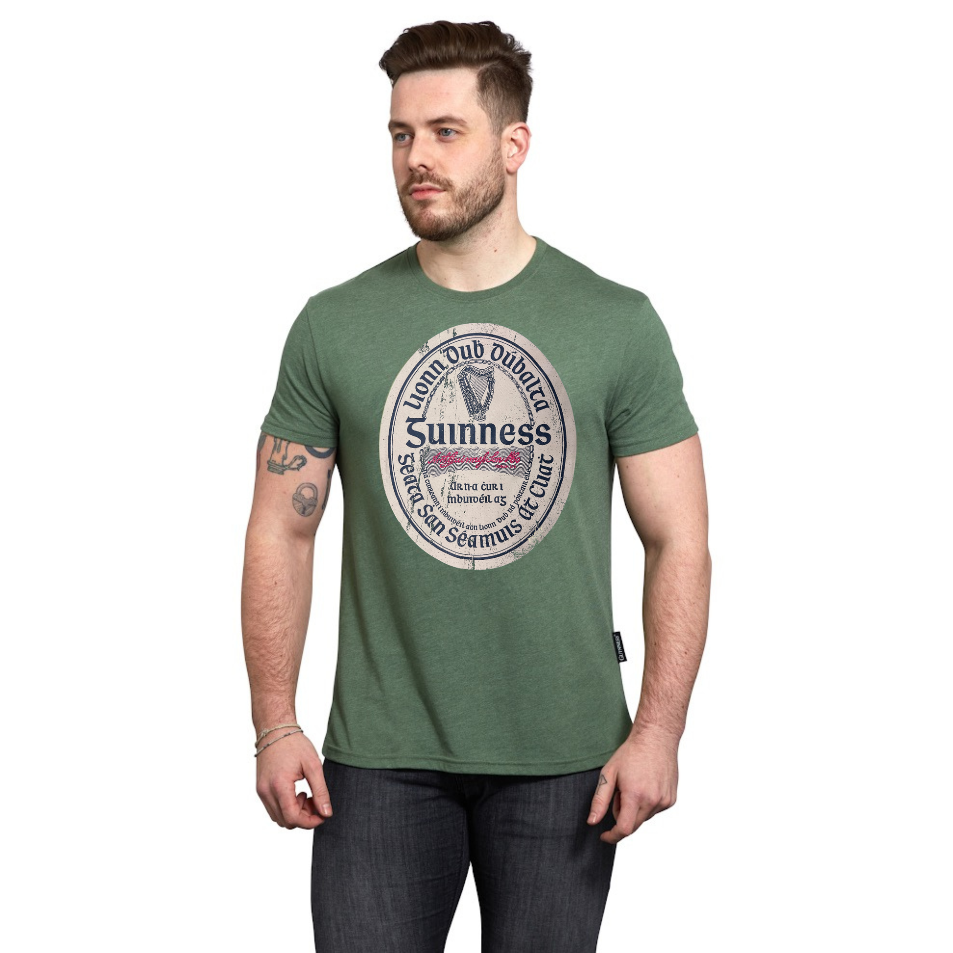 A man with short brown hair and a beard wears the Guinness Green Distressed Label Tee, a cotton blend unisex graphic t-shirt with a circular logo, standing against a plain white background.
