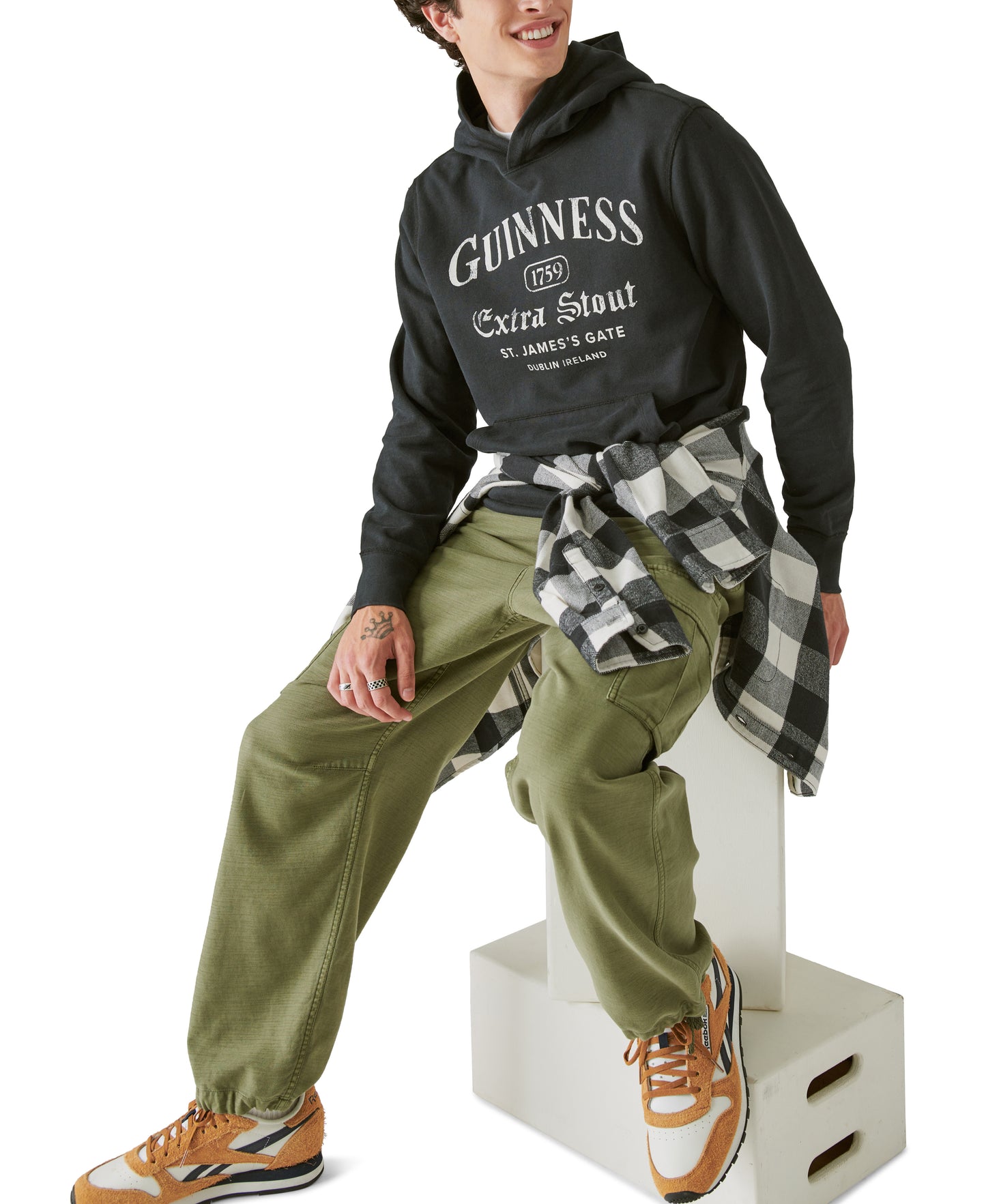 A man wearing a Guinness Logo Hoodie sitting on a box from the Guinness Webstore US.