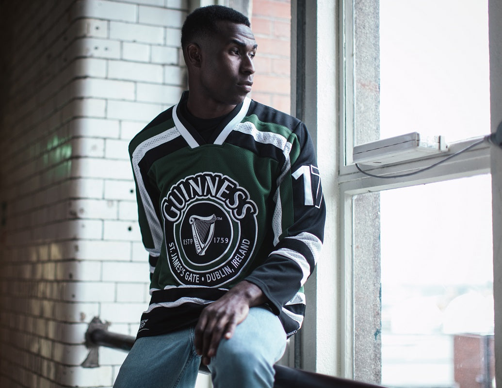 A young man in a Green & White Hockey Jersey with the Guinness harp logo.