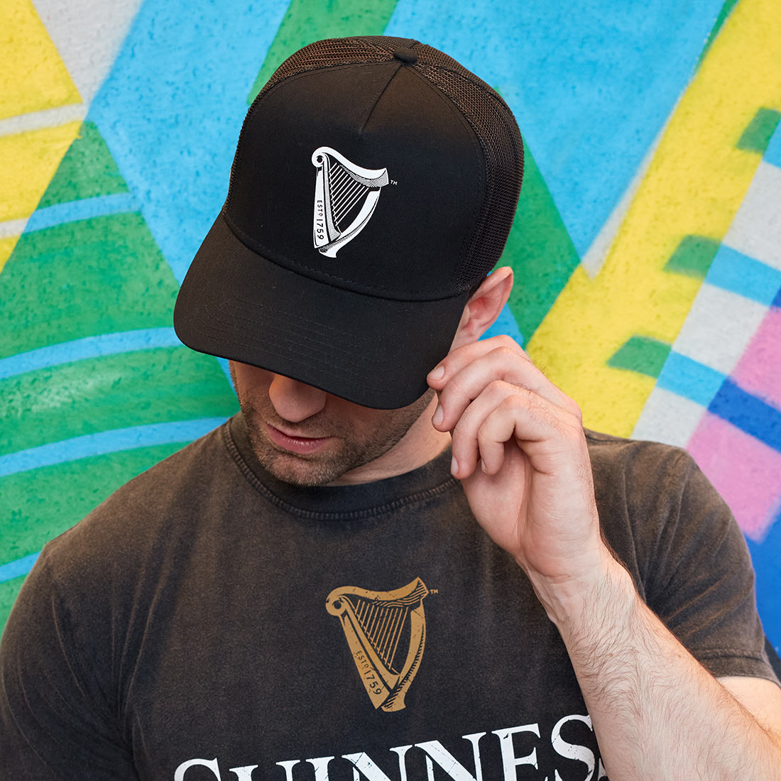 A man wearing a Guinness Premium Black & White Cap in front of a colorful wall.
