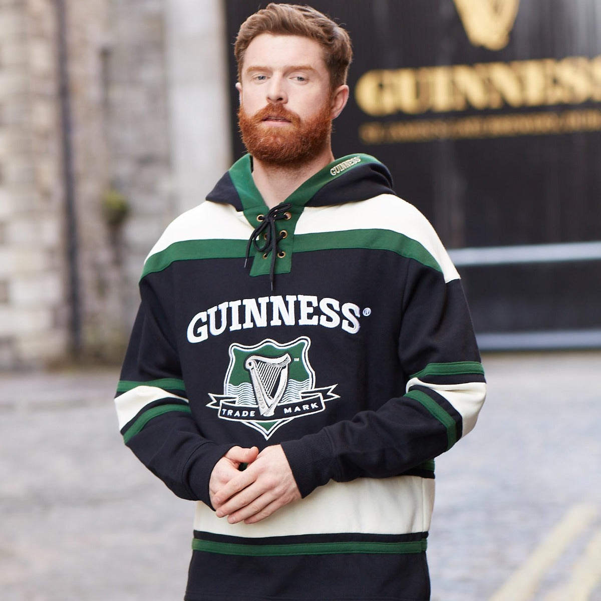 A man wearing a Guinness Green Hockey Style Hooded Sweatshirt made of heavyweight cotton blend.