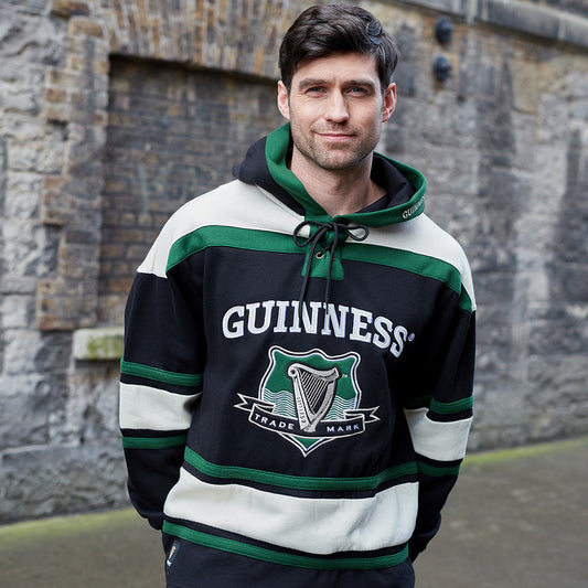Man wearing a Guinness Green Hockey Style Hooded Sweatshirt, made of heavyweight cotton blend material, standing in front of a brick wall.