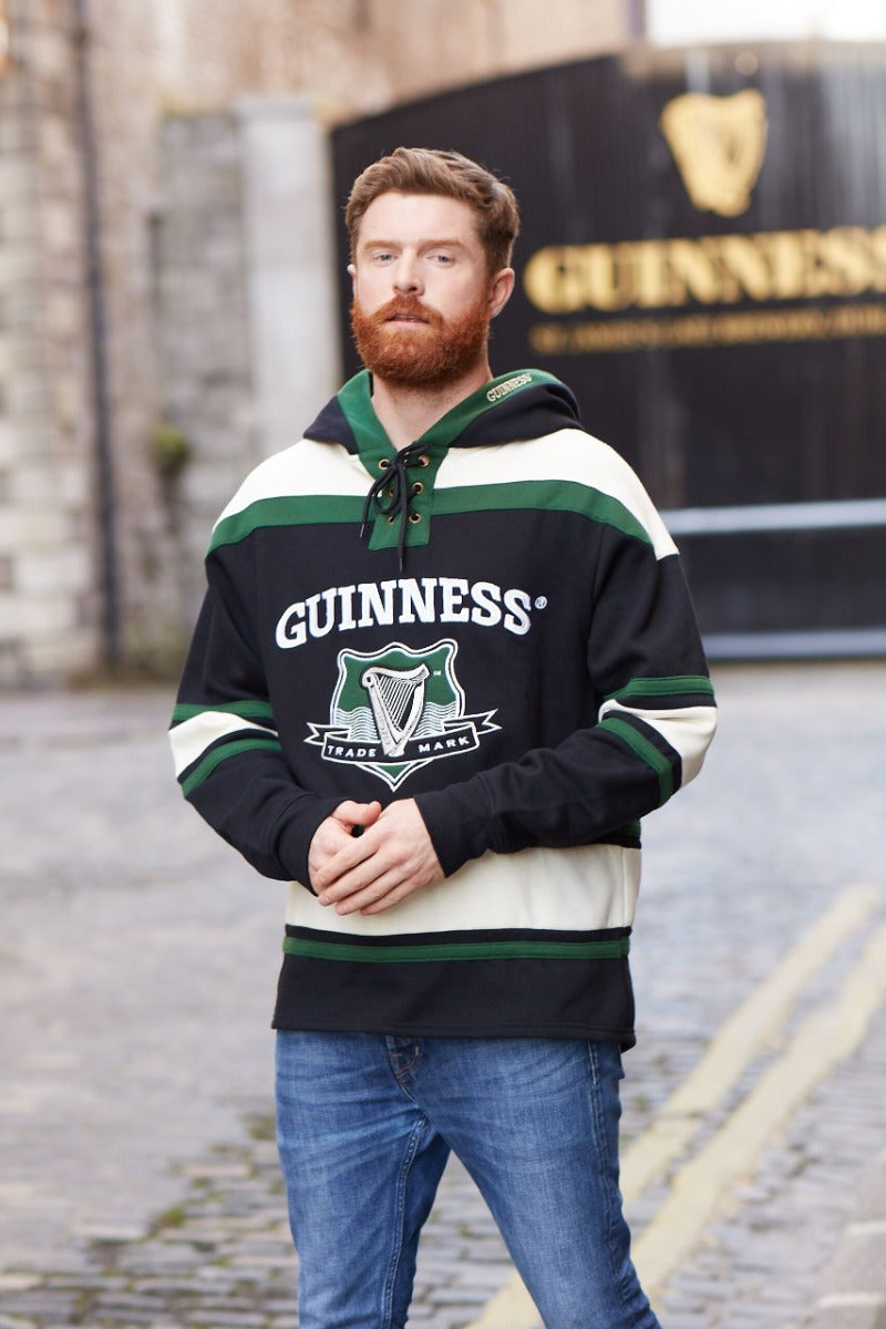 A man wearing a Guinness Green Hockey Style Hooded Sweatshirt, made of heavyweight cotton blend.