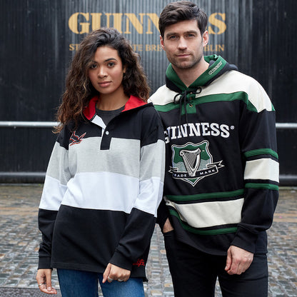 A couple standing in front of a Guinness sign wearing Guinness Green Hockey Style Hooded Sweatshirts.