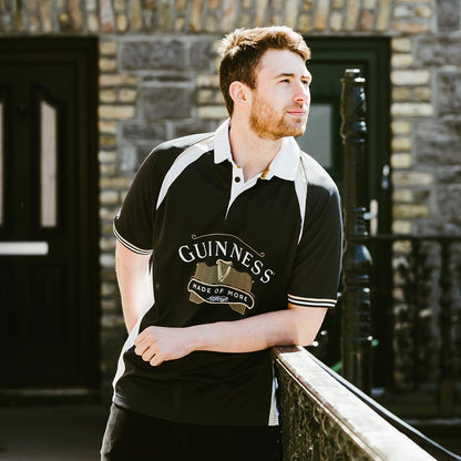 A man wearing a Guinness Made of More rugby jersey leaning against a railing.