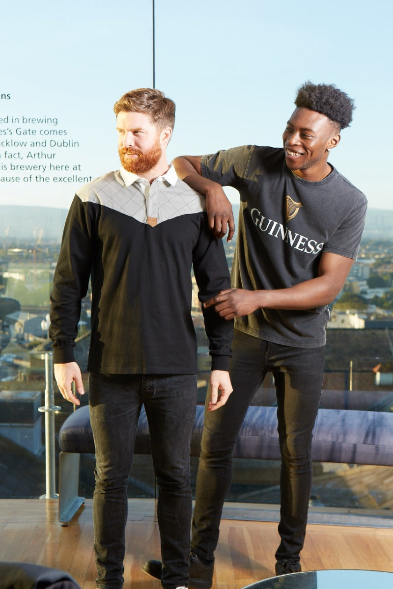 Two men wearing the Guinness Heritage Charcoal Grey & Black Long-Sleeve Rugby jerseys standing next to each other in front of a building.