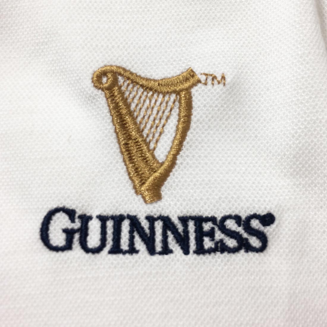 A Guinness Notre Dame Performance Polo Shirt White with a harp emblem.