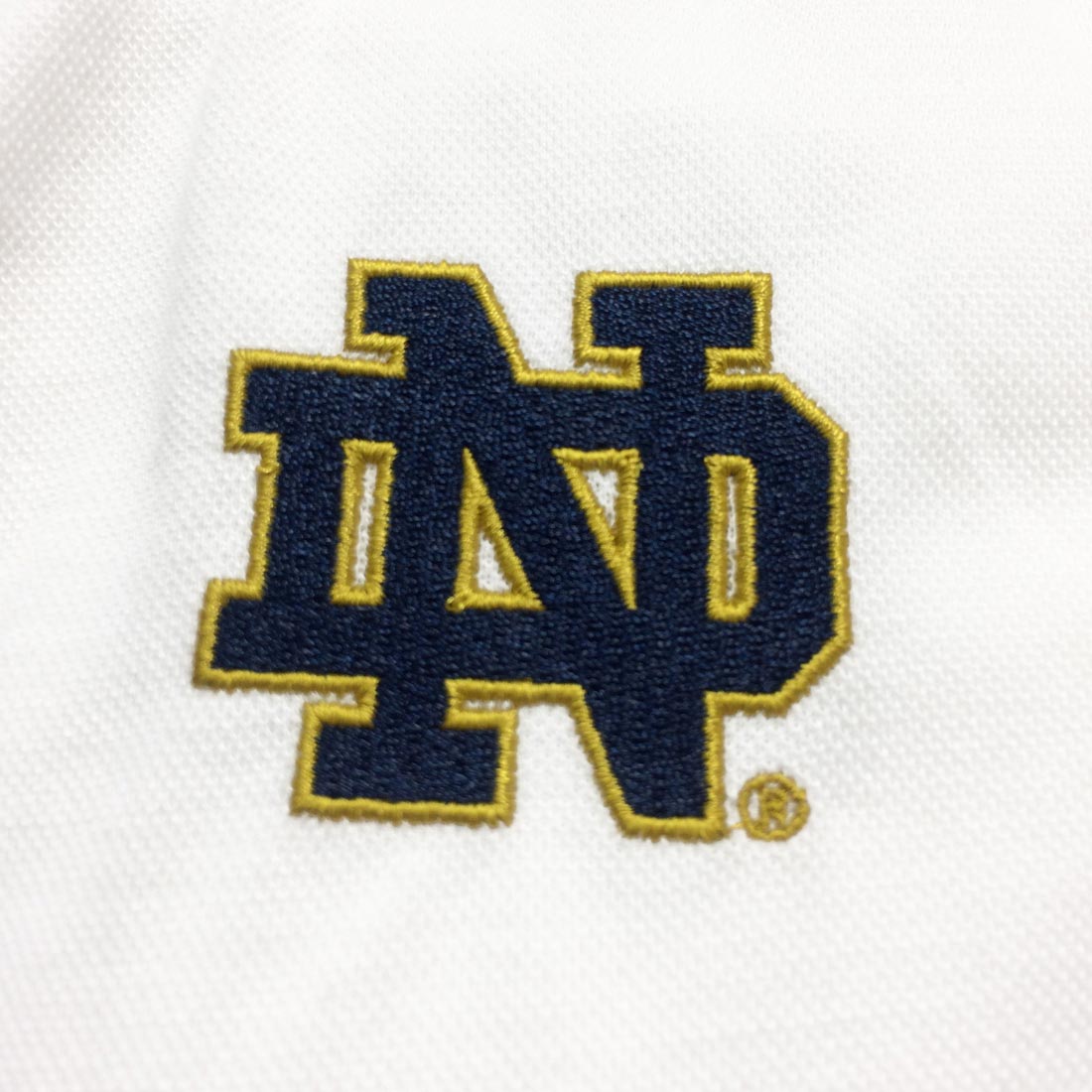 A close up of the Guinness Notre Dame logo on a Guinness Performance Polo Shirt White.
