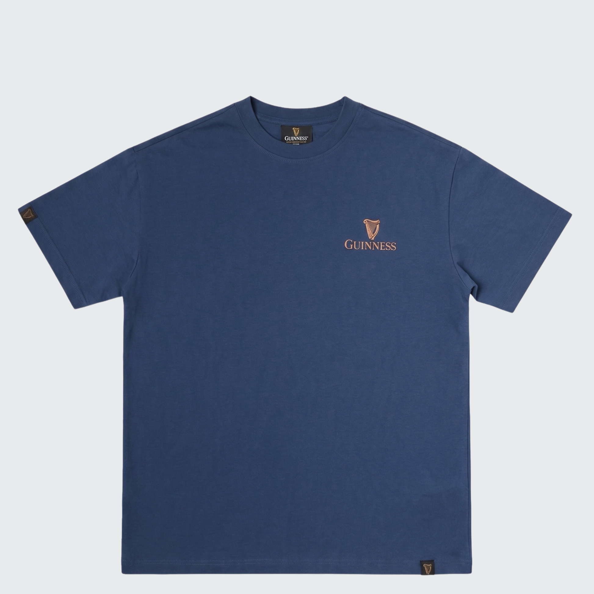 The Guinness Gilroy Seal Tee – Blue from Guinness Webstore US is a short-sleeve t-shirt featuring a small orange Guinness logo and harp emblem on the left chest. It is part of the limited edition Iconic Gilroy collection and is shown laid flat against a white background.