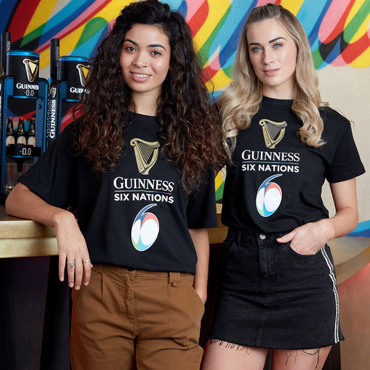 Two women wearing official Guinness Six Nations Black Tee t-shirts standing at a bar with beer taps in the background.