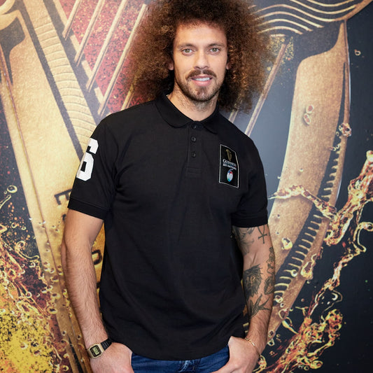 Man with curly hair wearing a Guinness Six Nations Black Polo Shirt, standing in front of an abstract patterned background.