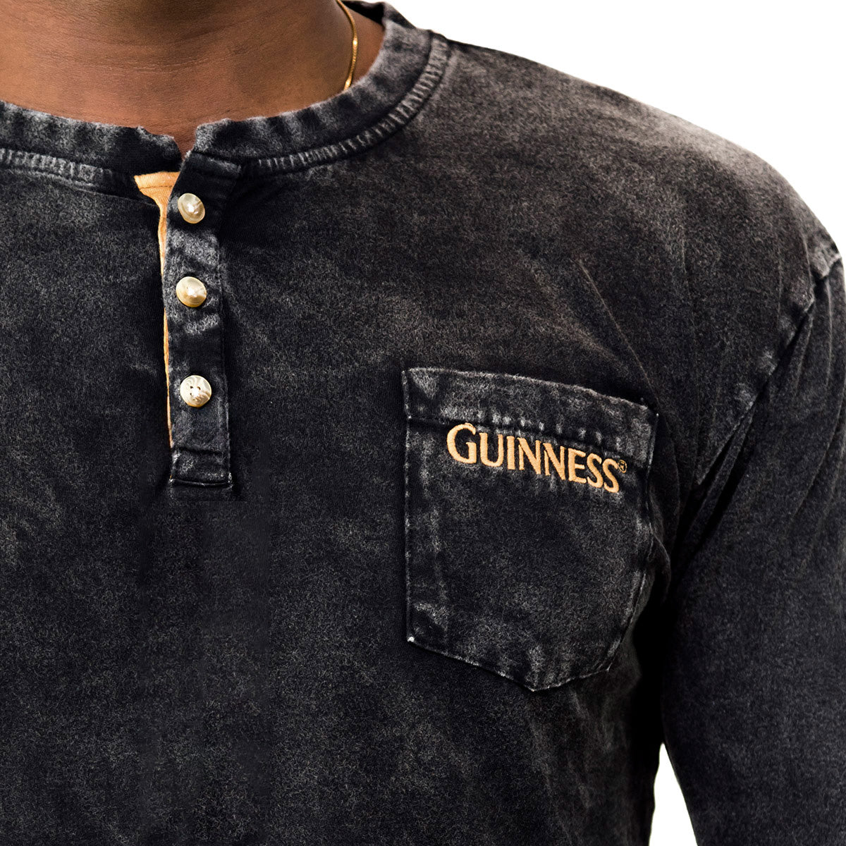 A close-up of a person wearing the Guinness Classic Washed Black Henley, a buttoned shirt with a pocket embroidered with "GUINNESS" in yellow, made from premium combed cotton for superior comfort.