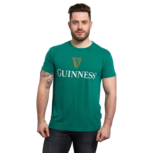 A Guinness lover with short hair and a beard stands against a white background, donning a green Green Guinness Harp Premium Tee from Guinness Webstore US.
