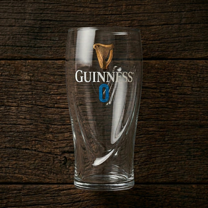 The Guinness 0 Gravity Pint Glass from Guinness Webstore US features the iconic logo and a bold blue zero, displayed against a dark wooden background.