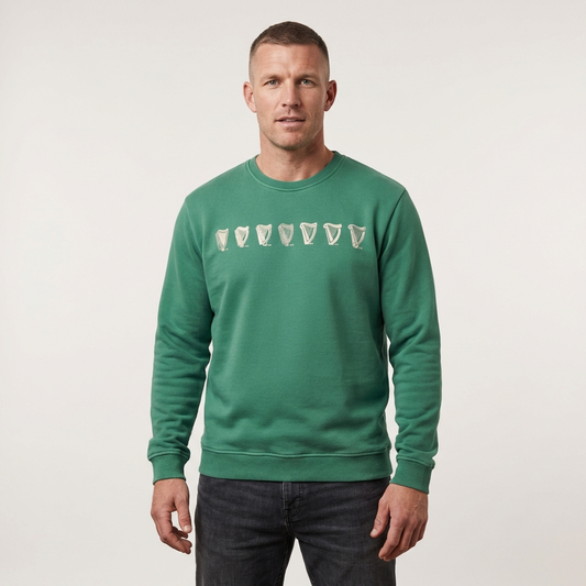 A man wears a Guinness Webstore US Evolution Harp Green Sweatshirt with stylized pint glass graphics across the chest, standing against a plain light background.