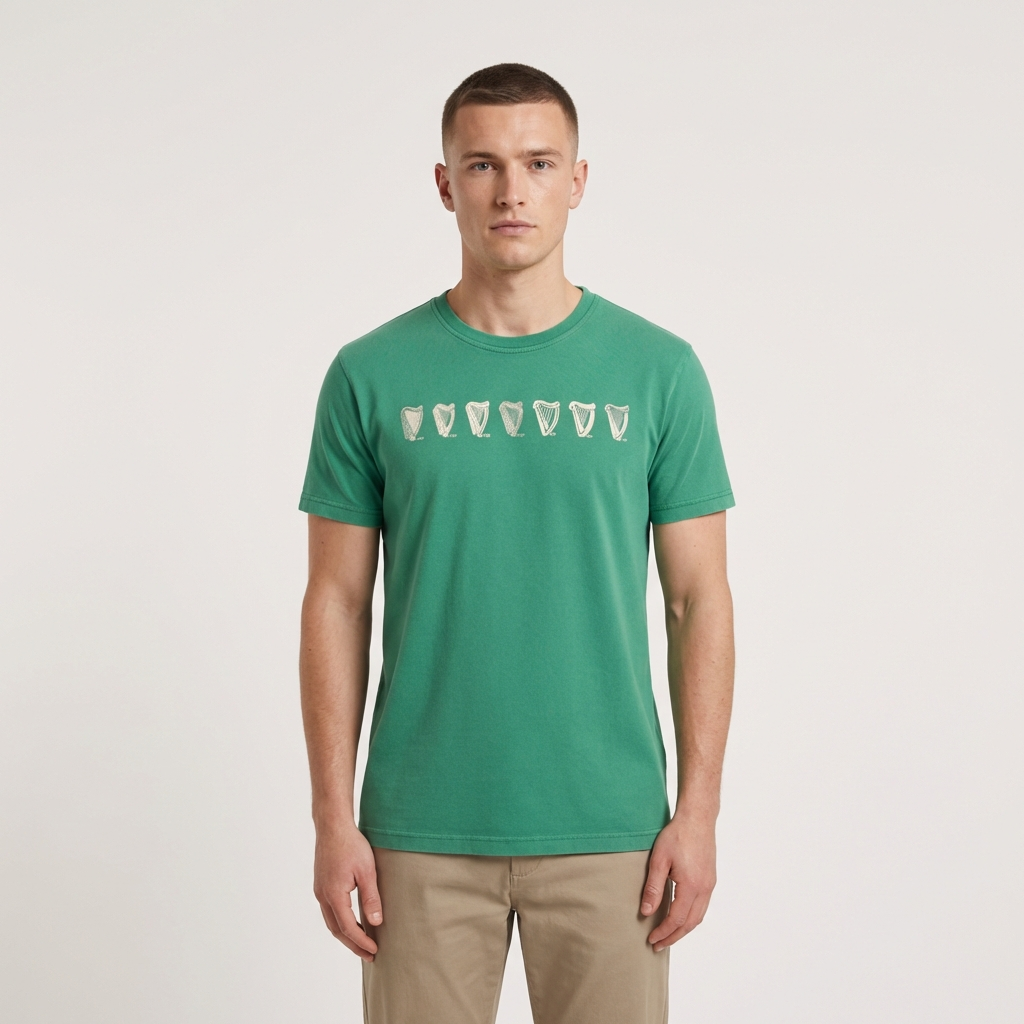 A man wearing a Guinness Green Evolution Harp Premium Tee, featuring white shark teeth graphics across the chest, stands facing forward against a plain white background.
