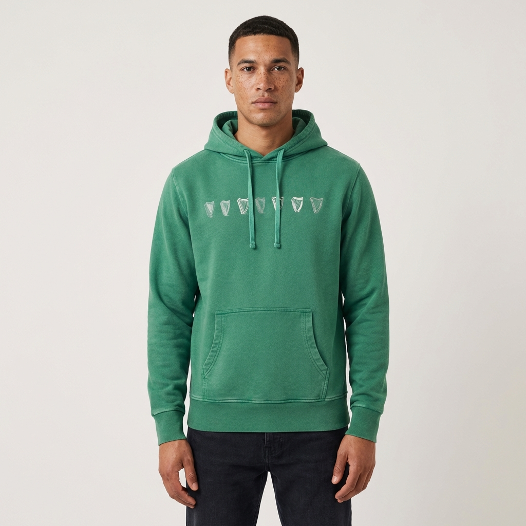 A person faces forward wearing the Guinness Evolution Harp Green Hoodie, which features a vintage look with a green kangaroo pocket and arrowhead design, paired with dark jeans against a plain background.