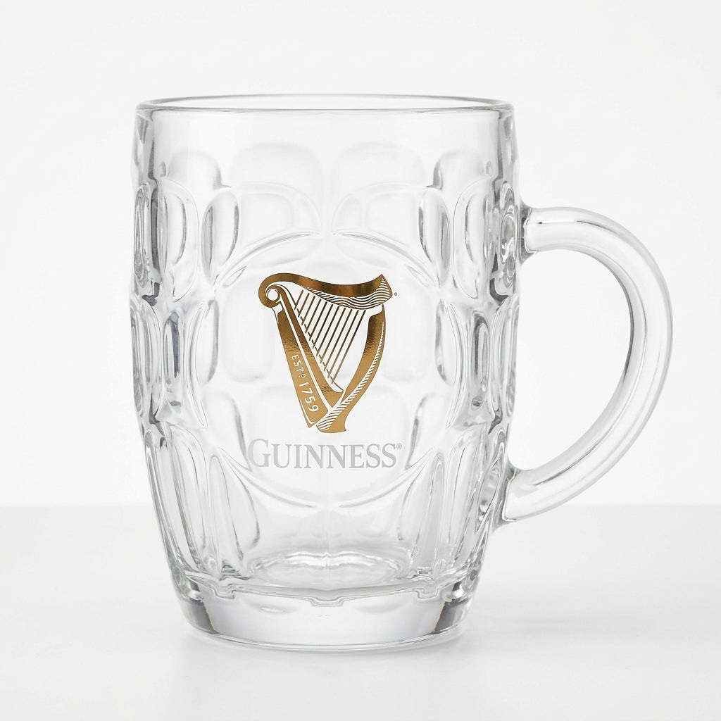 The Guinness Gold Harp Dimple Glass Mug – 20 oz Tankard from Guinness Webstore US features clear glass, a sturdy handle, and a gold harp with "Guinness" on the front—a classic Irish pub mug for your collection.
