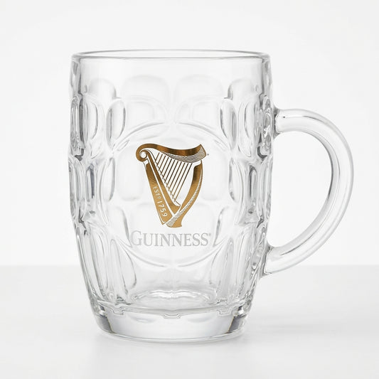 The Guinness Gold Harp Dimple Glass Mug – 20 oz Tankard from Guinness Webstore US features clear glass, a sturdy handle, and a gold harp with "Guinness" on the front—a classic Irish pub mug for your collection.