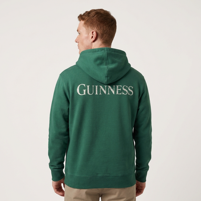 Someone wearing a green Evolution Harp Green Hoodie by Guinness, featuring "GUINNESS" in white on the back, faces away from the camera—an ideal pick for fans of vintage style and sustainable fashion.