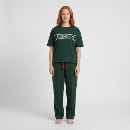 A person with long red hair stands barefoot in a Guinness Unisex 2-Piece Pajama Set – Green from Guinness Webstore US, against a plain white background.