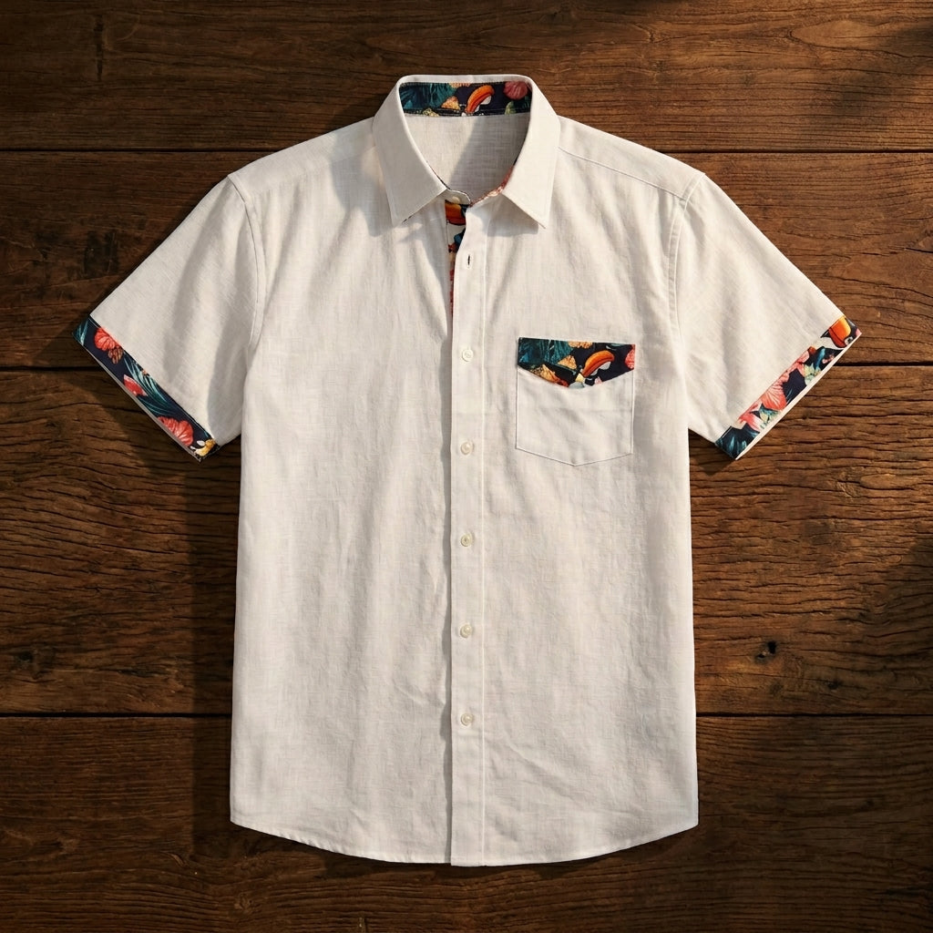 The Guinness White Linen Summer Shirt from Guinness Webstore US features short sleeves, a chest pocket, and floral-patterned lining on the collar, pocket, and sleeve cuffs. Displayed on a wooden surface.