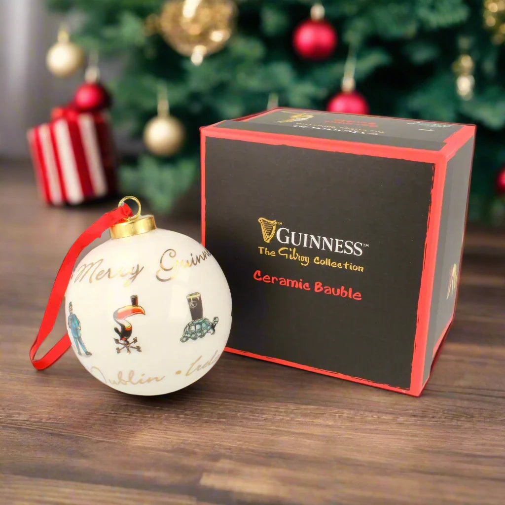 Guinness Gilroy Ceramic Holiday Bauble adorned with "Merry Christmas" text and festive illustrations, packaged in a black and red box from the "Guinness The Gilroy Collection" showcasing the iconic Guinness Toucan decoration.