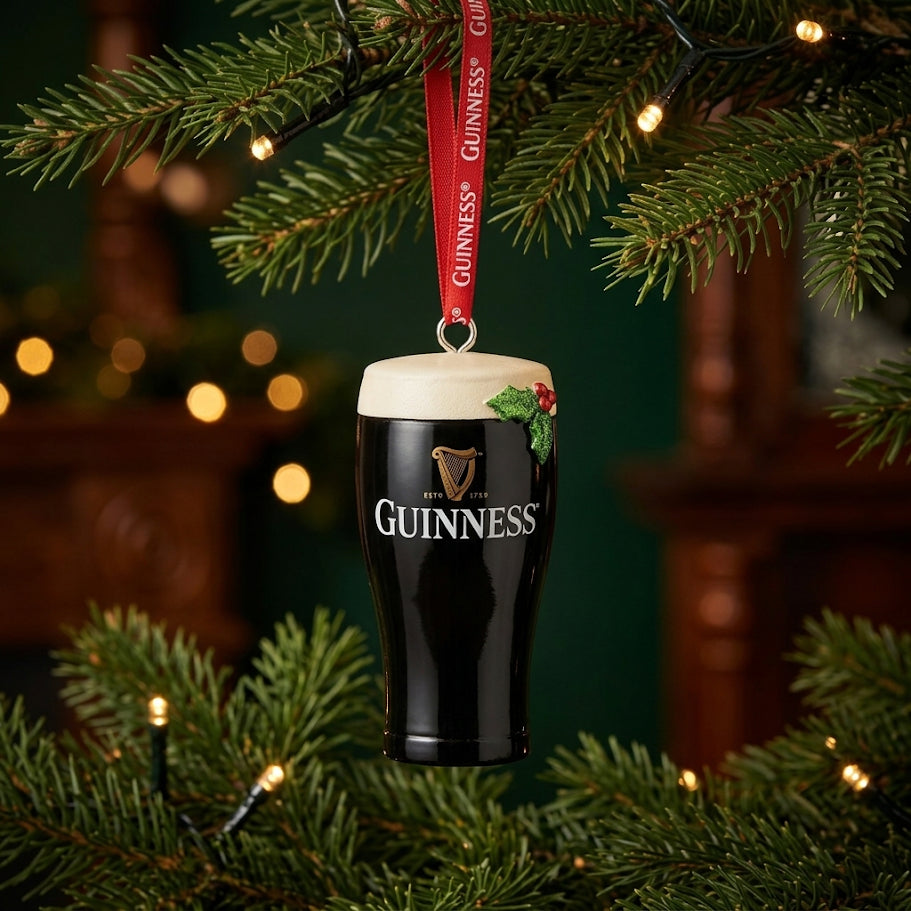 The Guinness Christmas Pint Decoration, expertly crafted from high-quality resin, hangs from a festive red ribbon on a beautifully decorated Christmas tree with twinkling lights—a standout addition to any Guinness holiday decor collection.